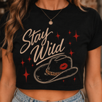 Close-up of a woman wearing a black Stay Wild cropped graphic tee with beige script, red star accents, and a cowboy hat illustration with leopard-print band.