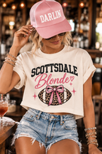 Woman wearing the Scottsdale Blonde crop tee with denim shorts and a pink Darlin’ Co. hat