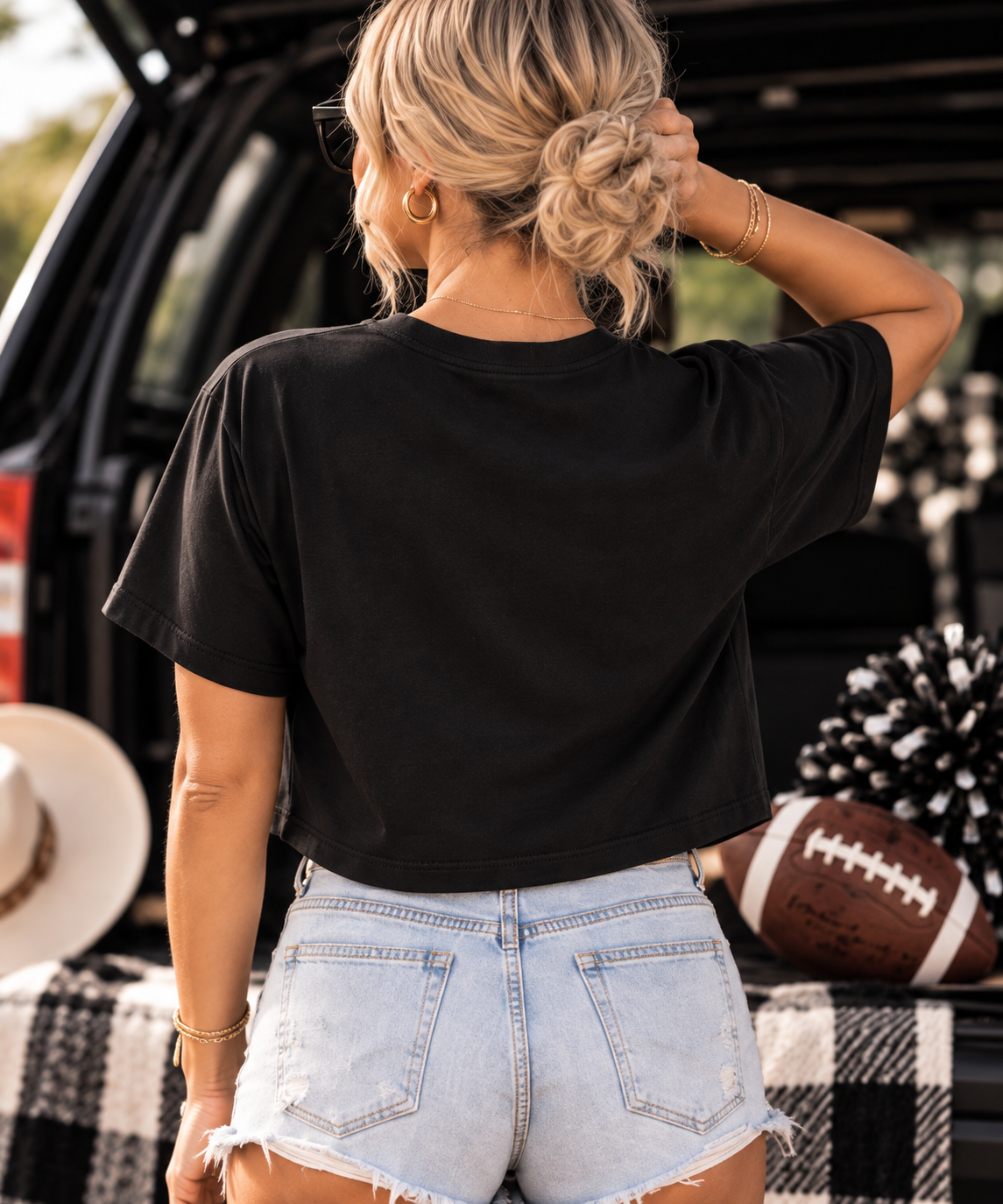 Back view: Back view of woman wearing the black Game Day crop tee with denim shorts
