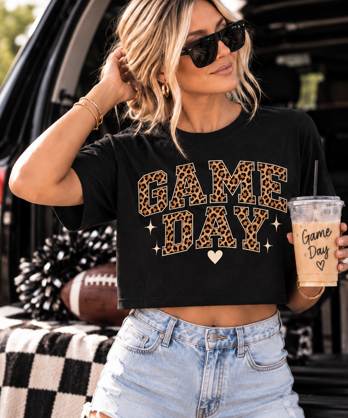 Woman wearing the black Game Day crop tee styled with denim shorts and sunglasses